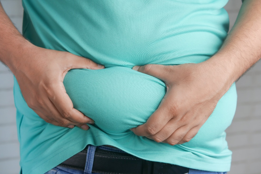 Person wearing a blue shirt holding onto a roll of their belly fat