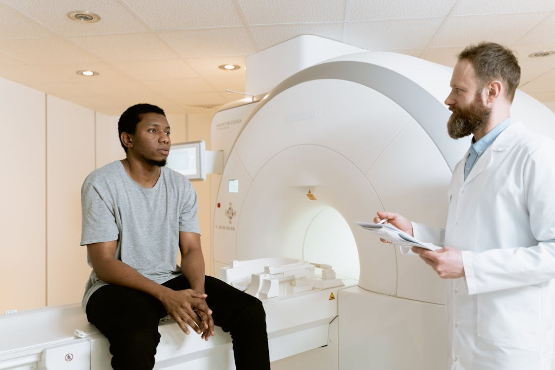 A man sitting on a CT scanner while the doctor guides him