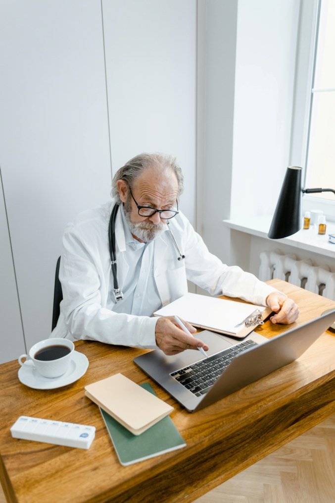 A man in a lab coat using his laptop on a brown wooden table