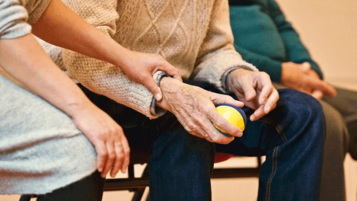 An older adult with wrinkled hands squeezes a stress ball.