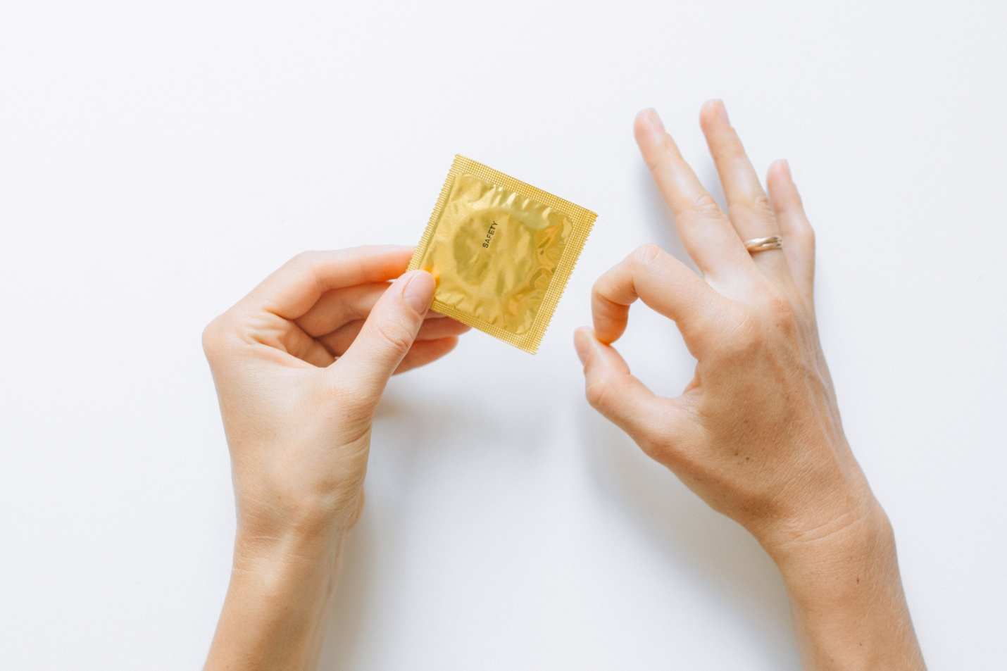 A pair of hands holding a wrapped condom in golden packaging