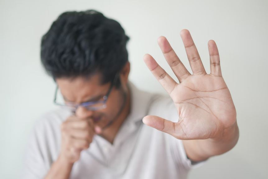 A man coughing and holding his palm up in front of his face