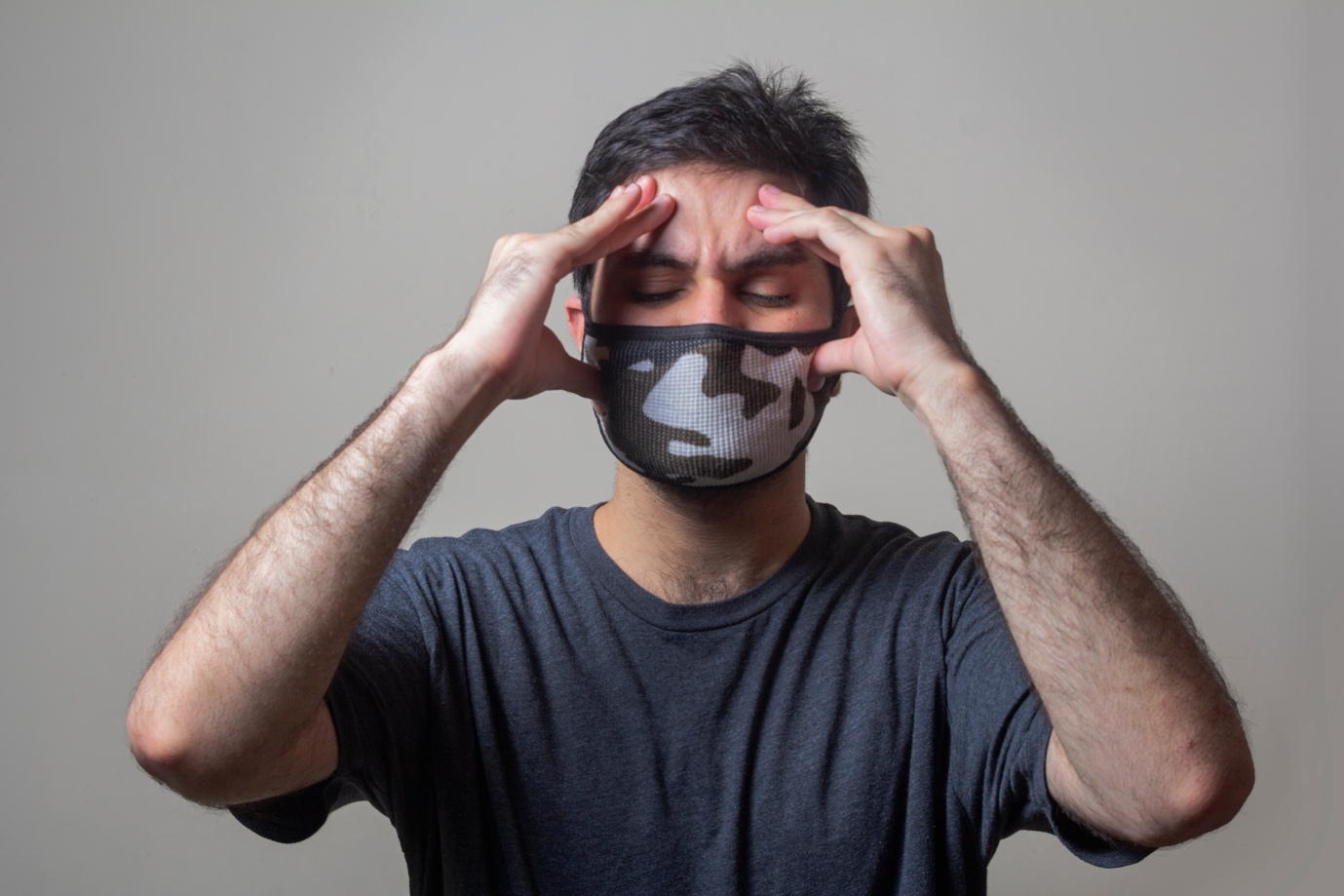 A man wearing a mask and holding his head due to a headache