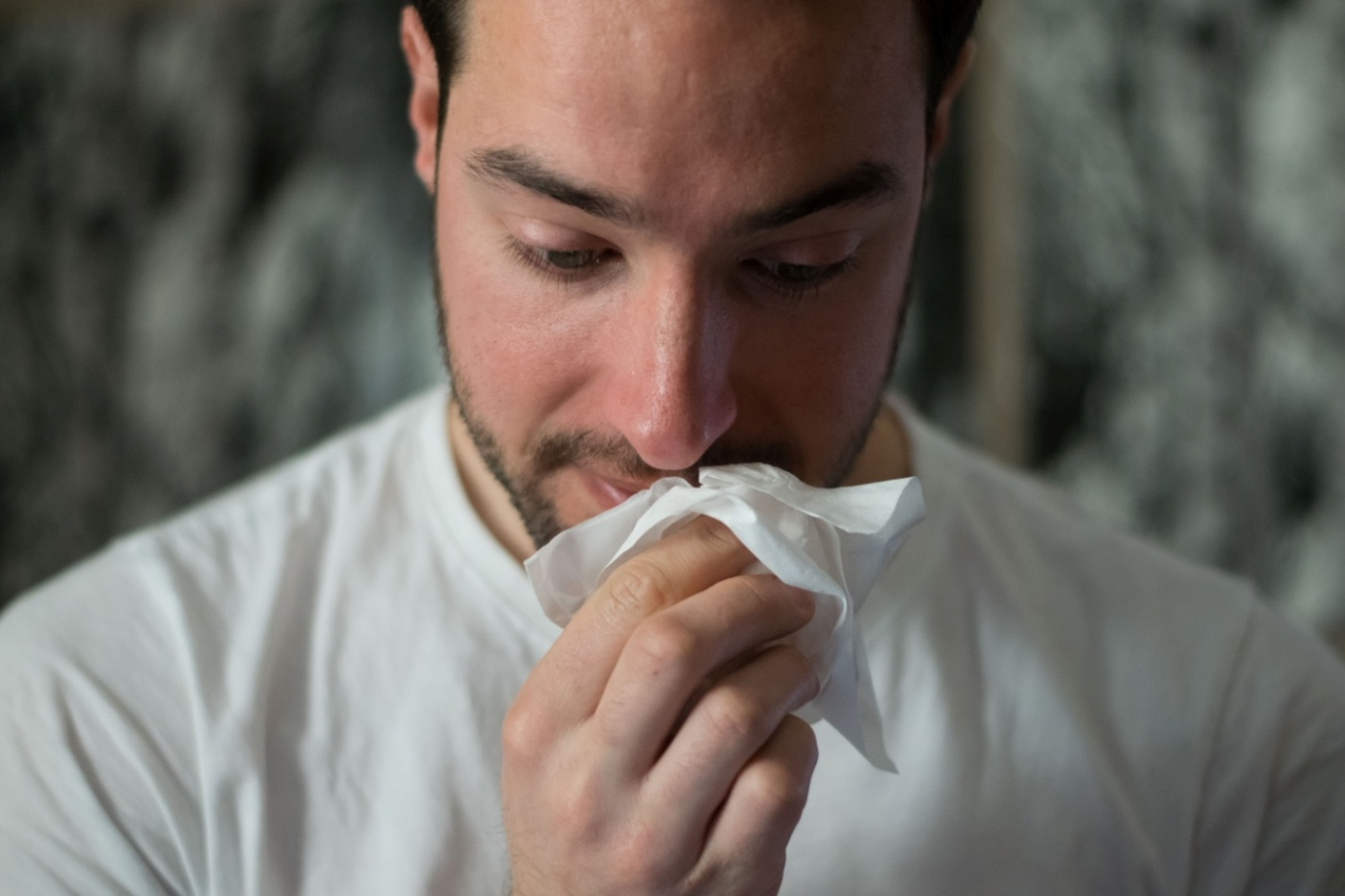 A man having a coldis holding a tissue close to his nose