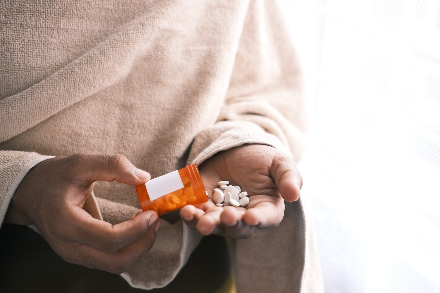 A person piling pills in their hands from an orange pill bottle
