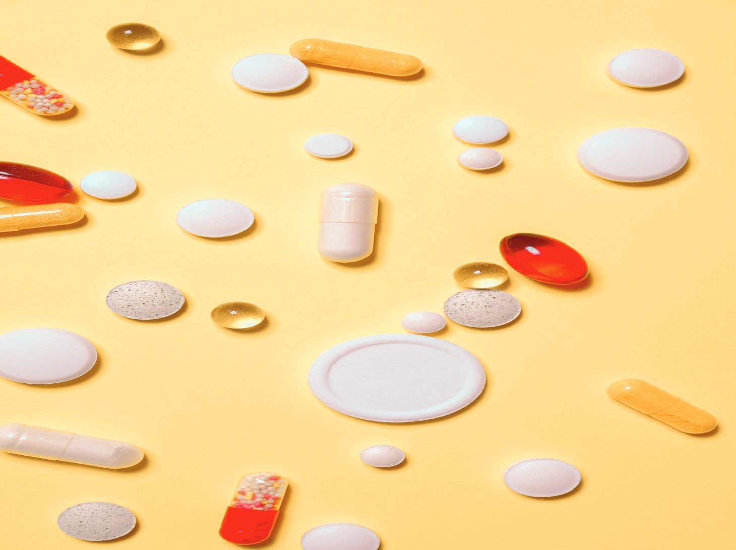 Red and white birth control pills scattered on a yellow surface.