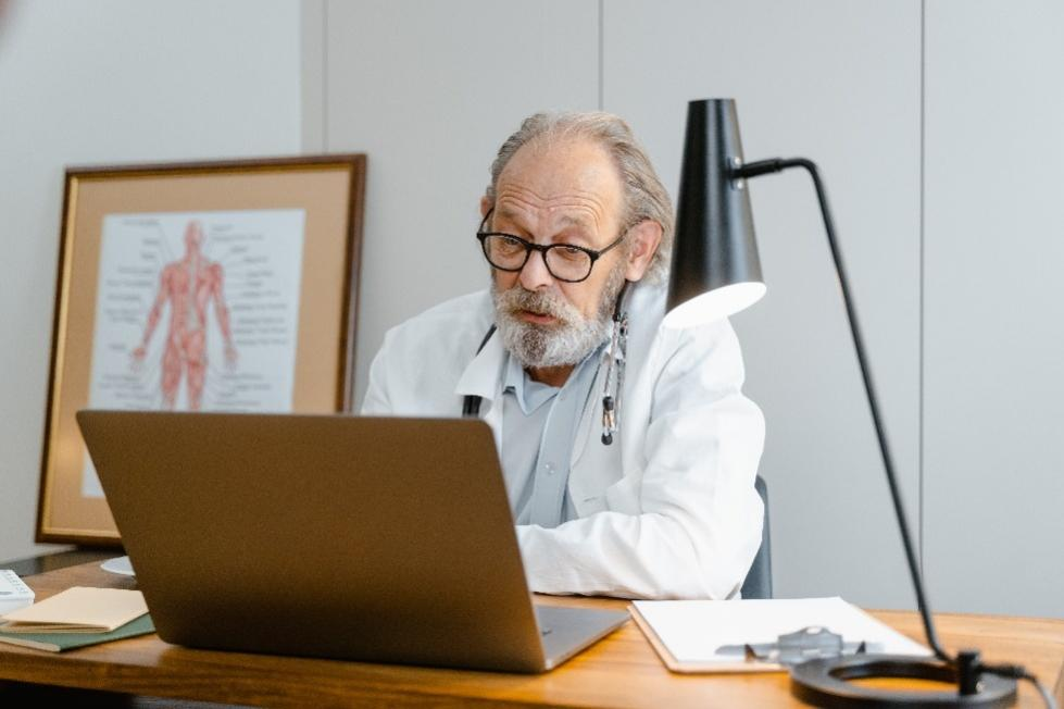 A doctor sitting in his office talking on his laptop