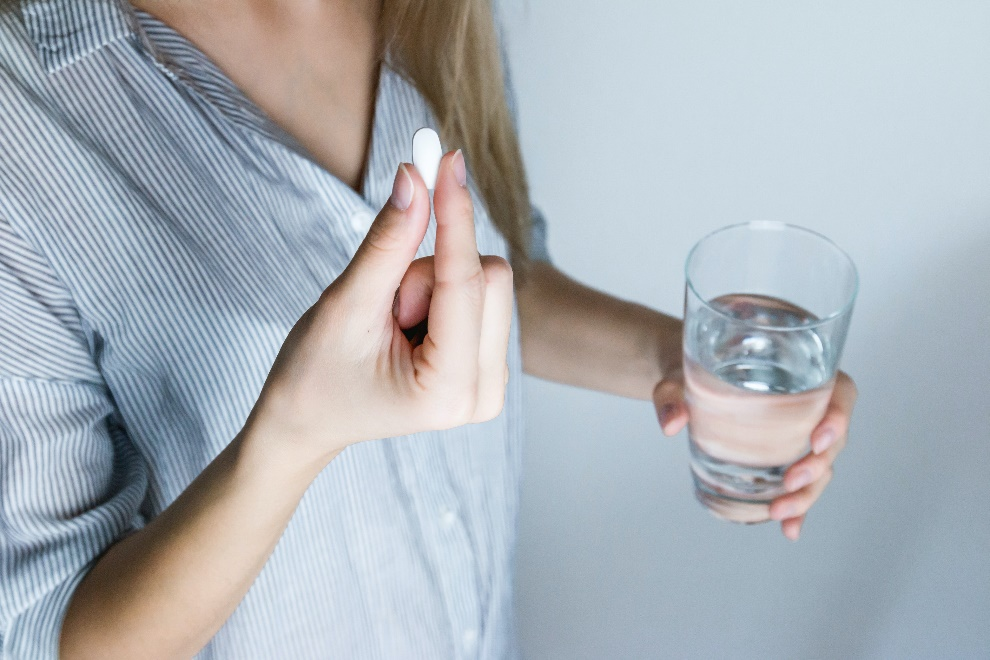A woman holding a glass of water and a white pill in her hands