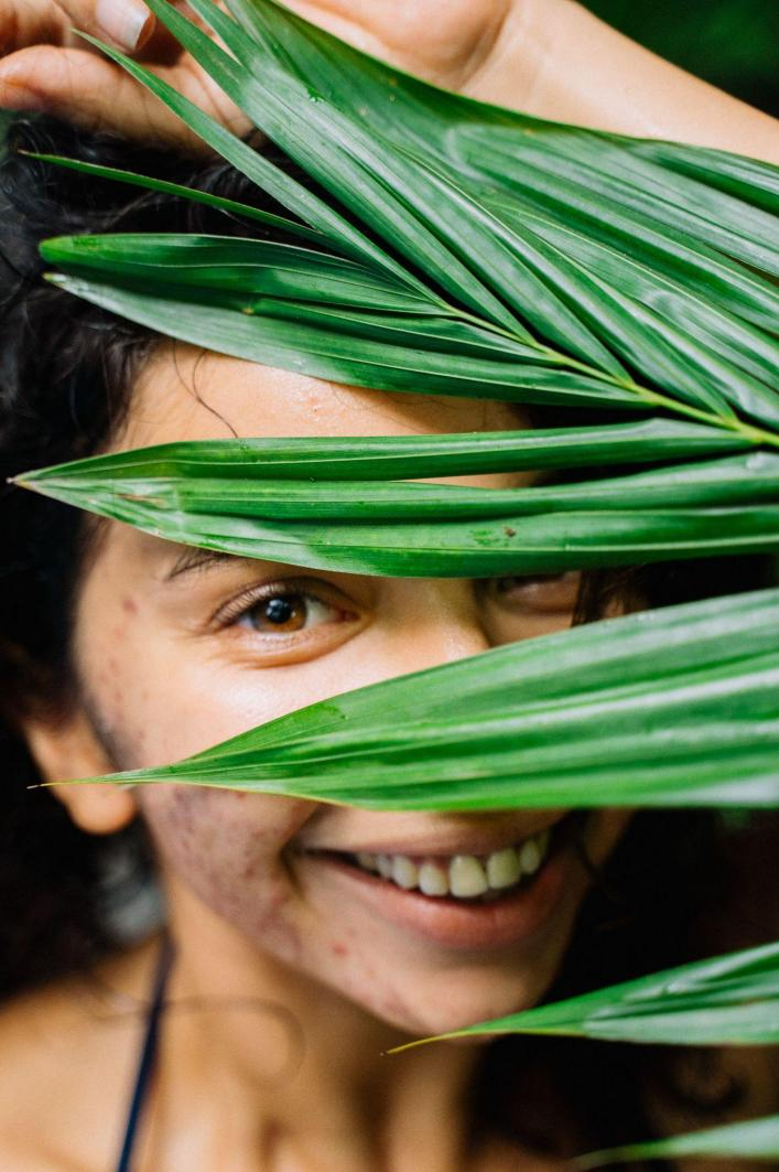Woman with cystic acne smiling behind leaves