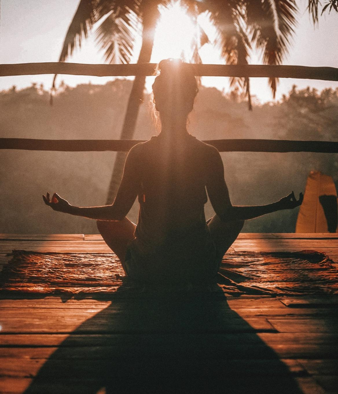 A woman meditating in the morning sun, sitting on a wooden floor in a yoga pose