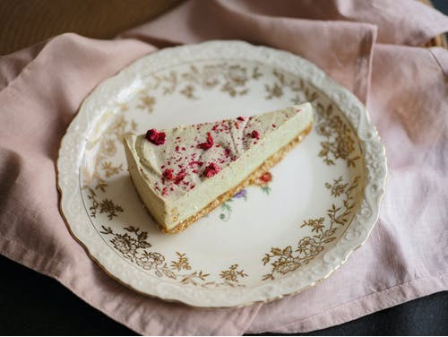 a slice of cheesecake sprinkled with red castor sugar on an ornamental plate