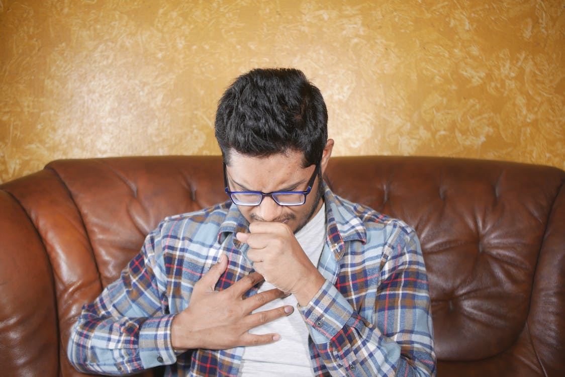 An image of a man coughing with a hand on his chest