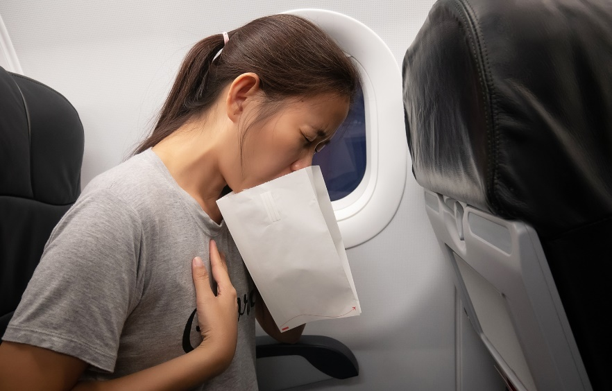 Female plane passenger vomiting in a paper bag