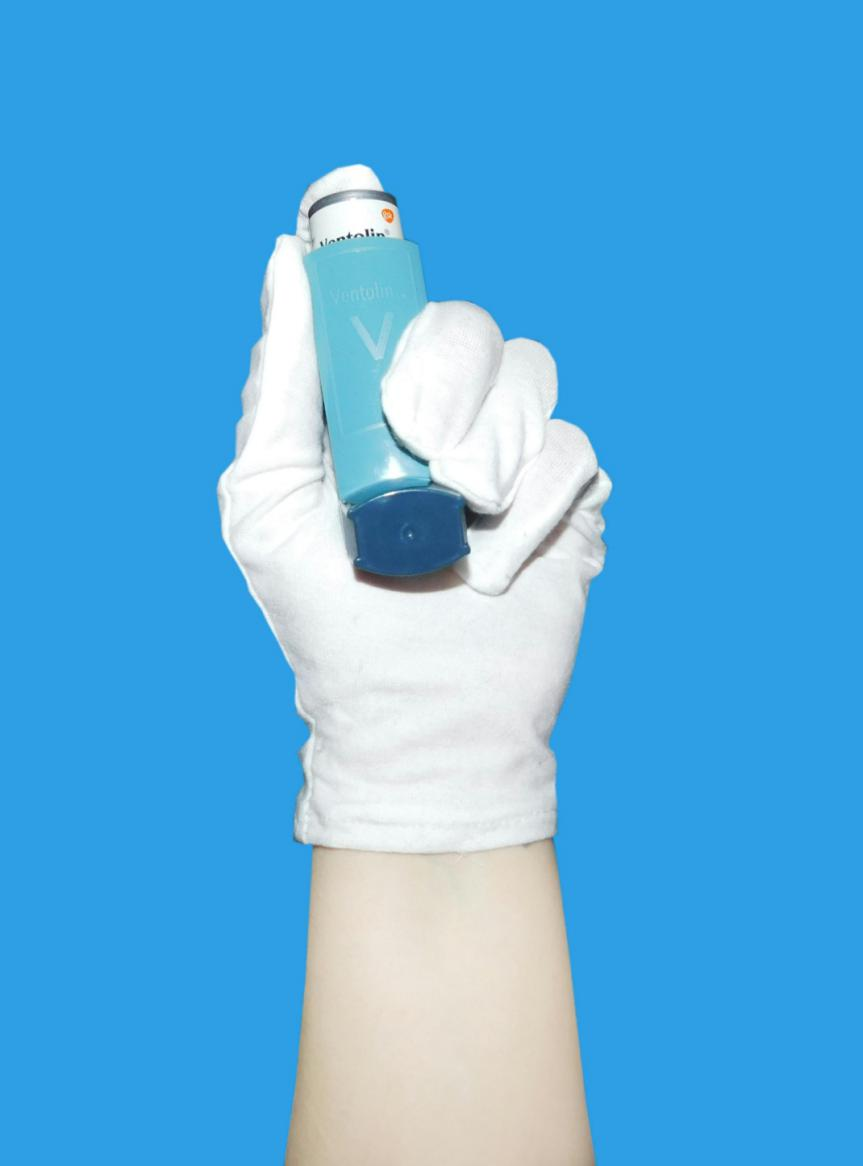 A hand with gloves holding an inhaler.