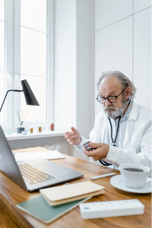 A photo of a man holding a stethoscope while looking at the laptop 