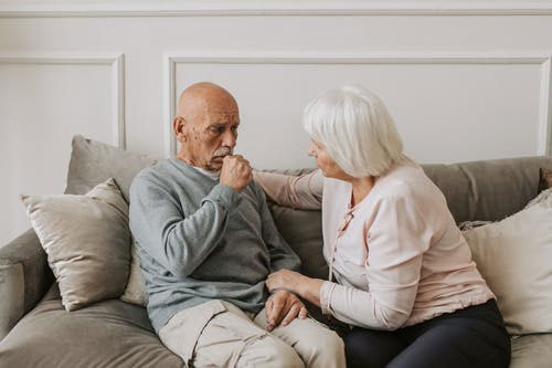 a woman helping a man in a grey sweater experiencing asthma symptoms