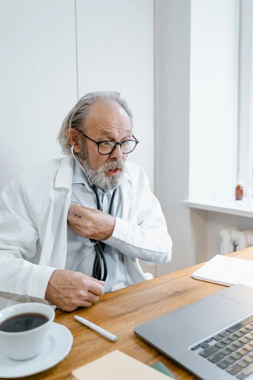 A photo of a man holding a stethoscope while looking at the laptop 