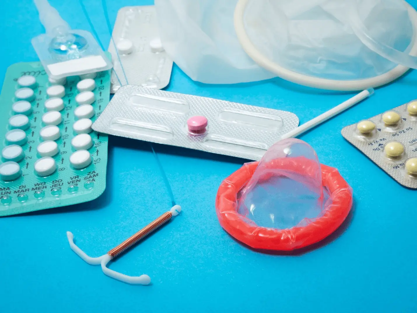 Pills sitting on a blue surface surrounded by a condom