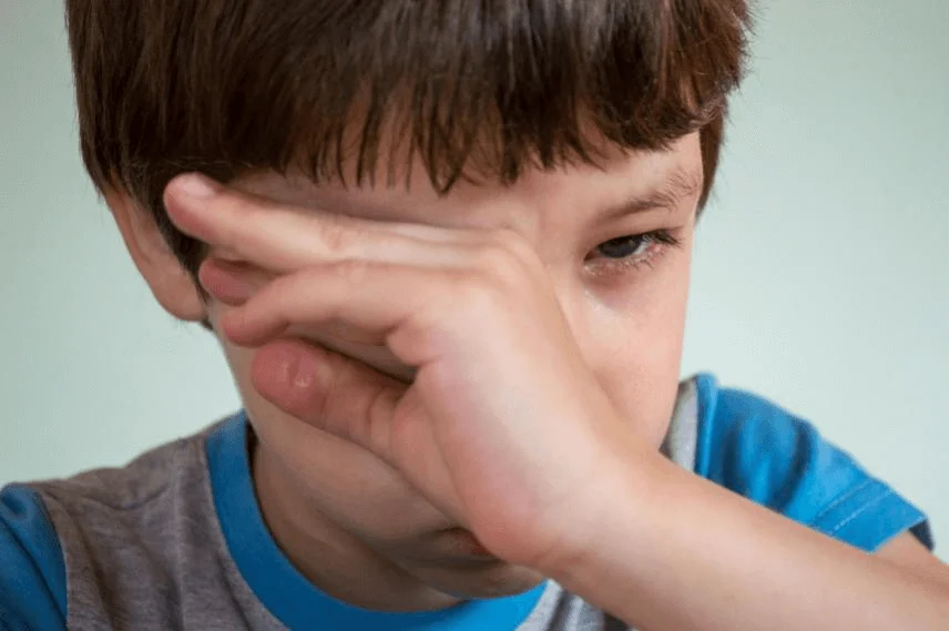 Boy rubbing his eyes, showing signs of irritation due to pink eye.