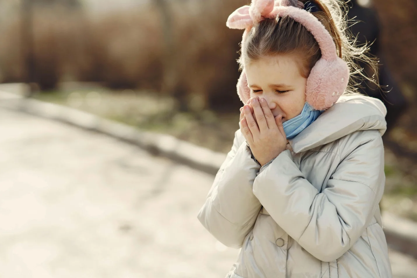 Young girl wearing earmuffs and a winter coat covering her nose and mouth.