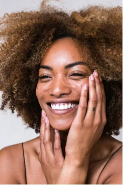 a woman smiling, holding her face