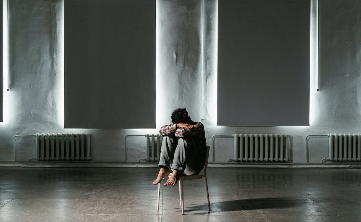 A man is sitting on the chair crouched due to pain caused by balanitis
