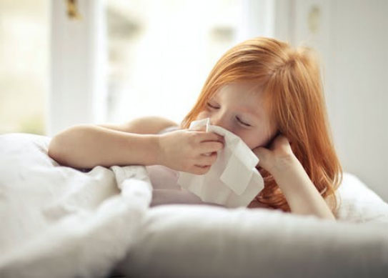 Sick girl wiping her nose while lying in bed