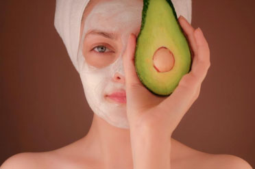 A person with a face pack on, holding an avocado