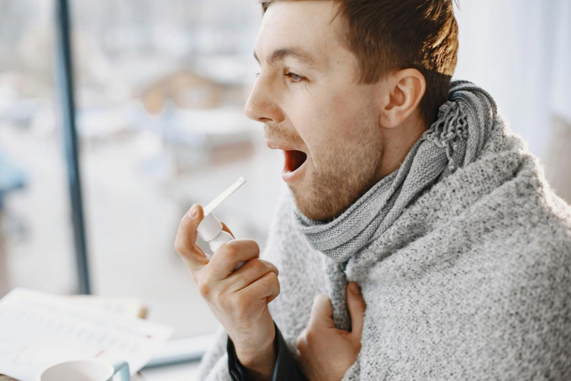 A person holding up cough medication near their mouth