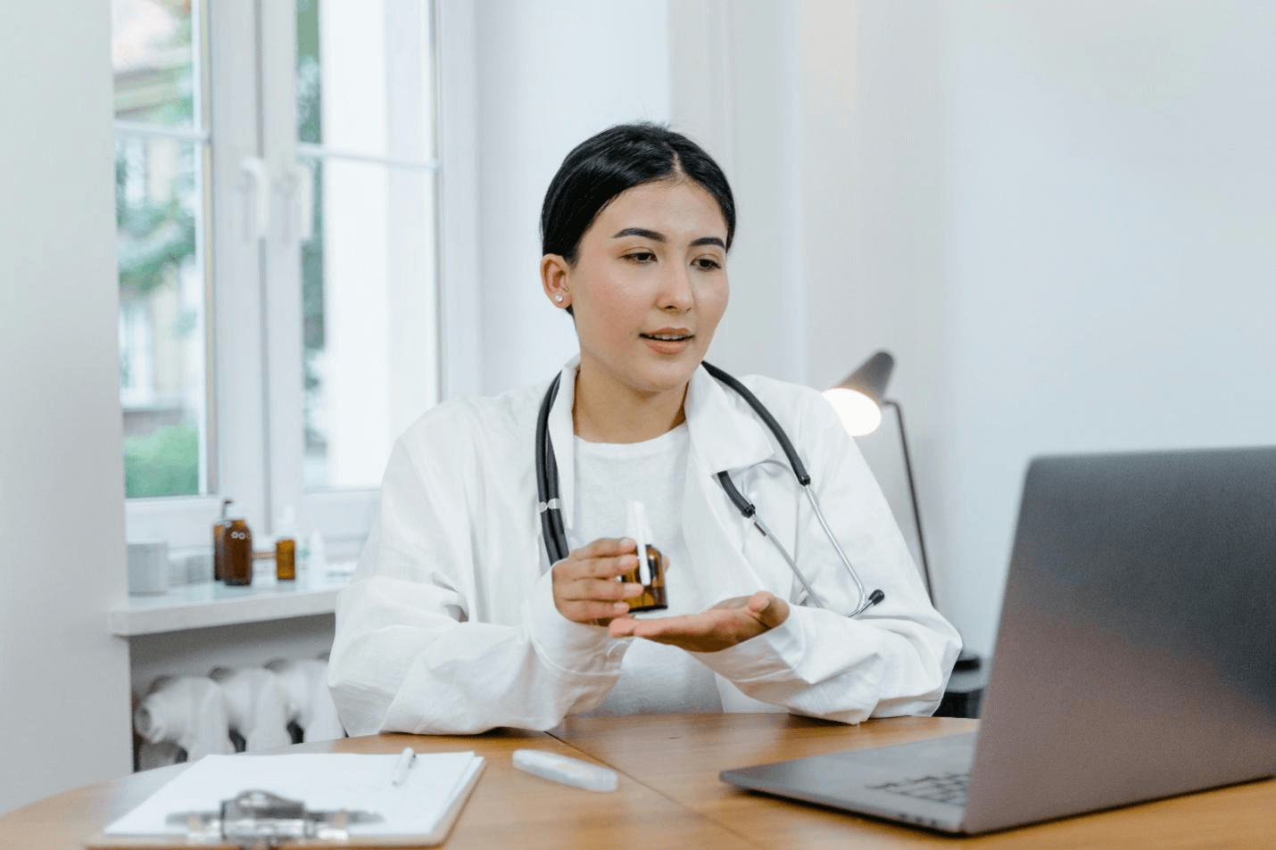 a doctor holding a small bottle in front of a laptop