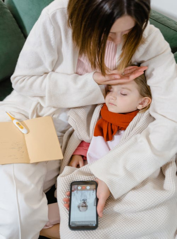 A woman embracing a sick child while speaking to a doctor online