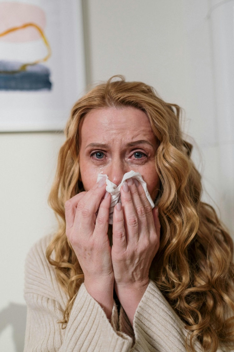  A woman covering her mouth with a tissue while sneezing.