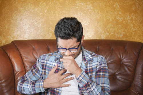 Middle-aged man coughing and holding his chest, showing early symptoms of bronchitis during winter