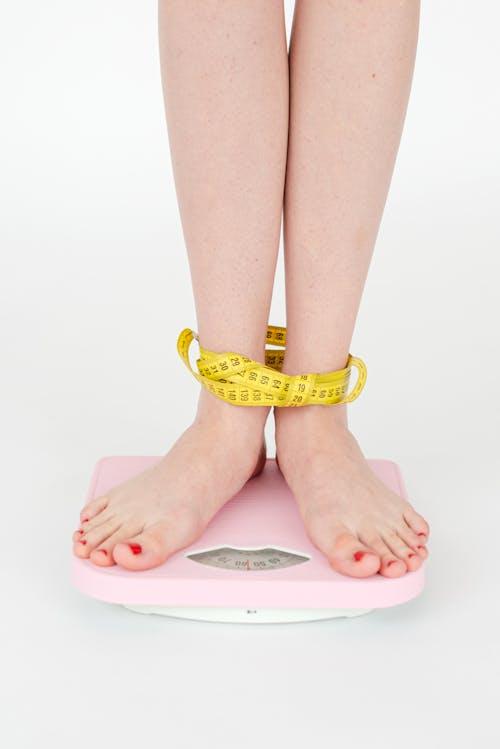 Person standing on a weight scale with measuring tape wrapped around their feet.