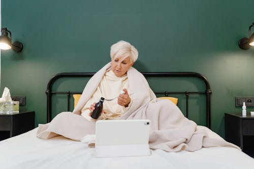 Woman in bed holding medicine and using a tablet for an online doctor consultation