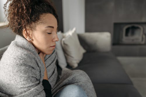 Woman wrapped in a blanket, appearing unwell with cold symptoms.