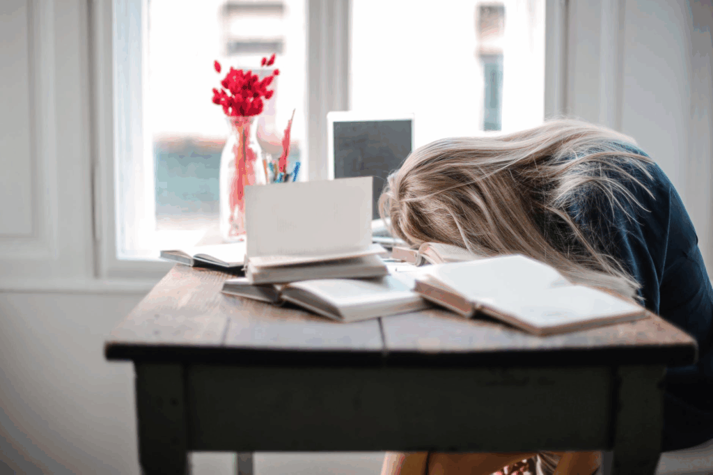 Woman resting her head on a desk, appearing exhausted from illness.