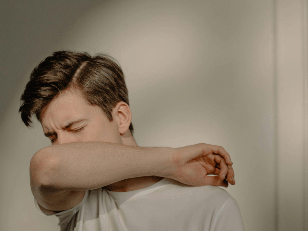 a man covering his mouth with his arm while sneezing