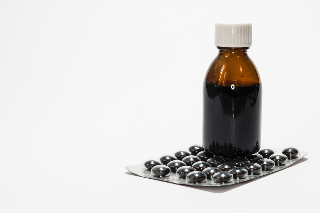 Cough syrup bottle and pack of tablets arranged on a white surface.