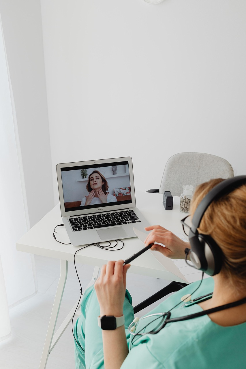 Doctor wearing a headset consulting a patient through a laptop during a virtual appointment.