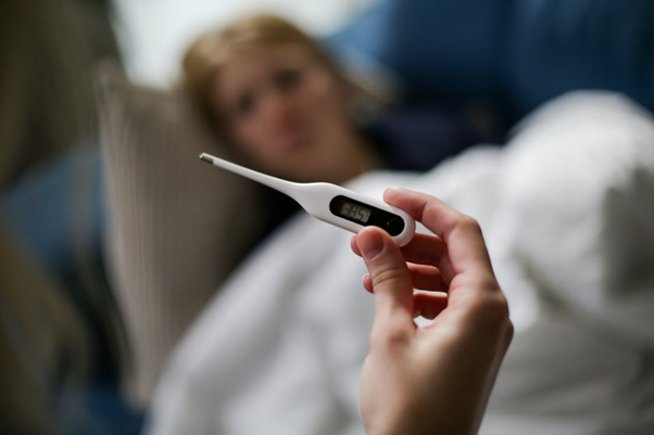 Person holding a thermometer showing a temperature reading