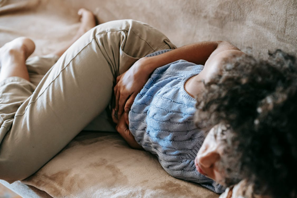 Woman sitting indoors holding her stomach while experiencing pain