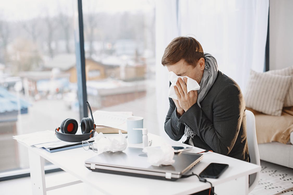Ill man sitting at a desk while sneezing