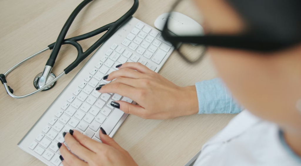 This image shows a doctor typing on keyboard with a stethoscope nearby.