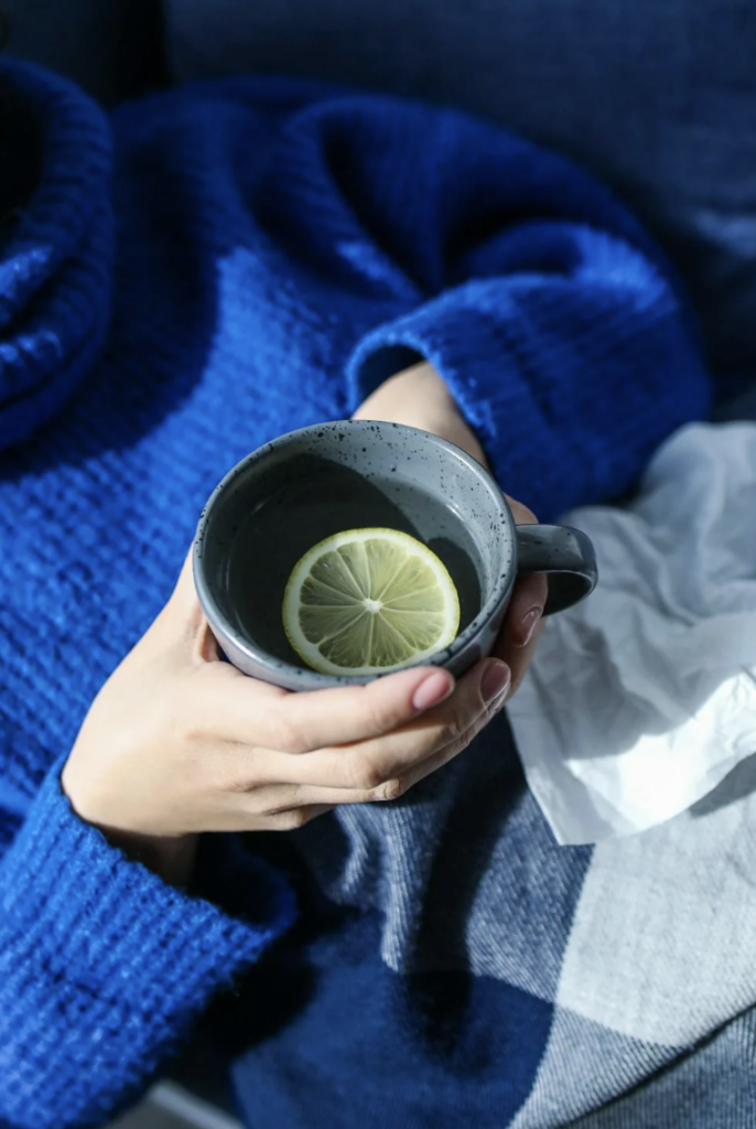 This photo shows a person holding warm tea beside lemon and tissues.