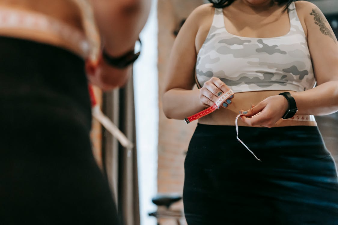 A woman measuring their stomach with the help of a measuring tape.