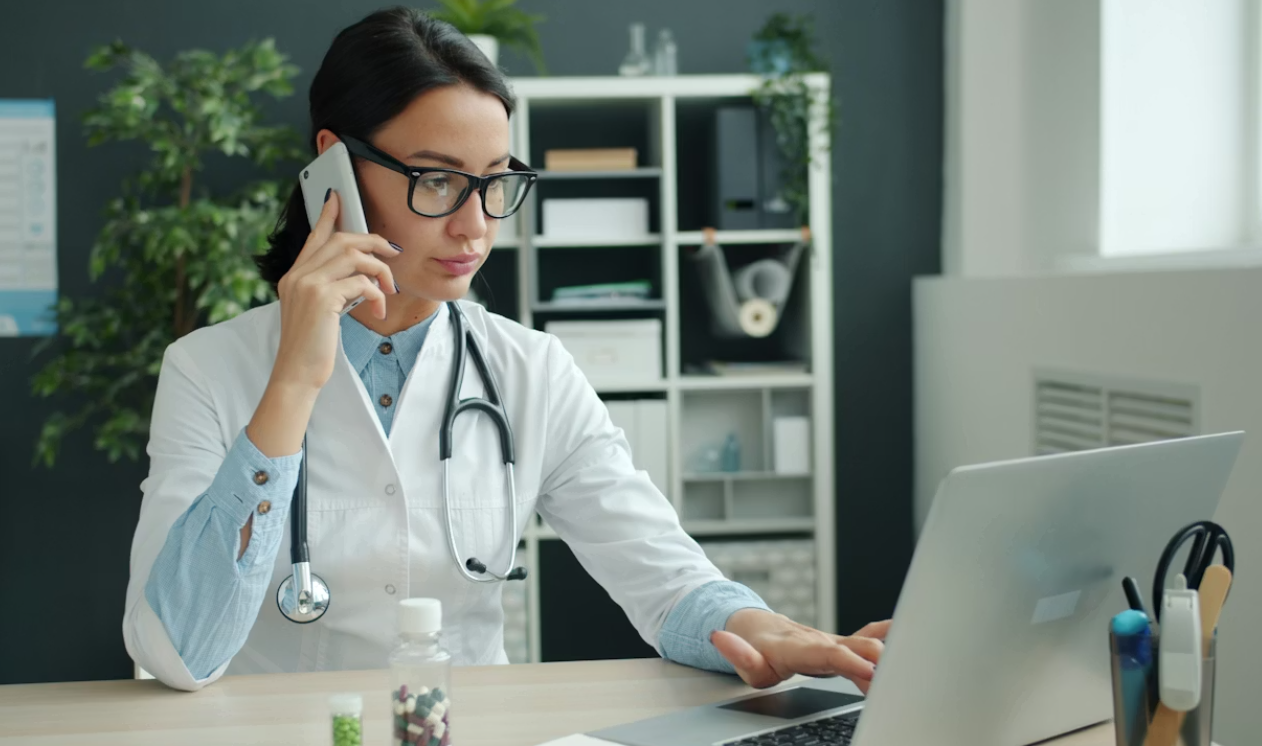 This image shows a doctor on the phone while working on a laptop.