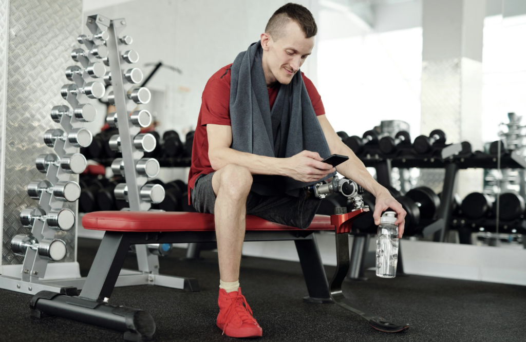 This photo shows a man sitting with a towel and water bottle in gym.