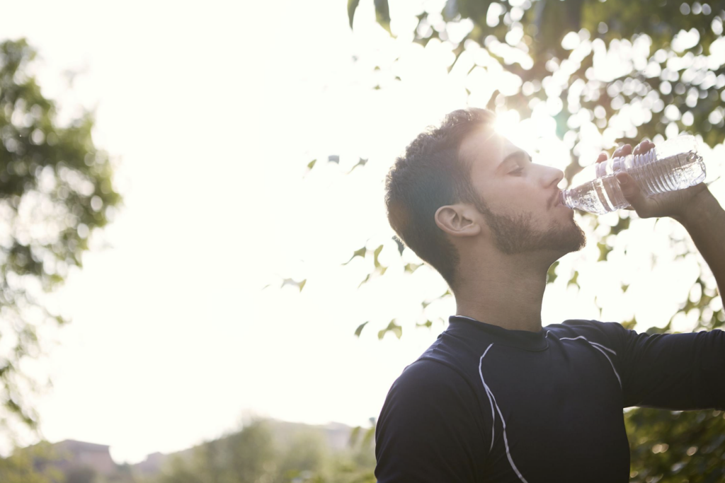 This photo shows a person drinking water from a clear bottle outdoors.