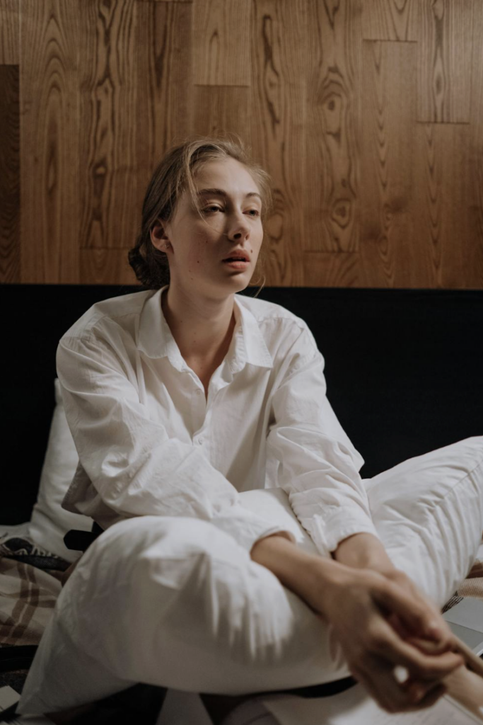 This photo shows a woman sitting on a bed with tired posture